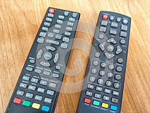 A pair of TV remotes laying next to each other. Two Television Remote Controls Side by Side on a Wooden Table. Partial