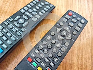 A pair of TV remotes laying next to each other. Two Television Remote Controls Side by Side on a Wooden Table. Partial