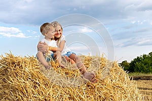 Pair of two cute adorable little caucasian sibling kids enjoy sitting on haystack bale and hug together at country