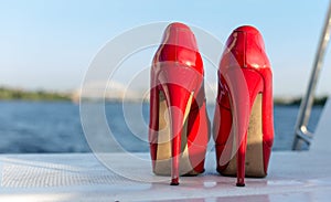 Pair of used red high heel women shoes on yacht desk.