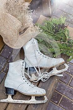 Pair of vintage white Ice Skates lying on the bench with fir-tree branches