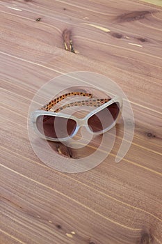 Pair of vintage woman sunglasses with white frames, rhinestones, centered, neutral wood background