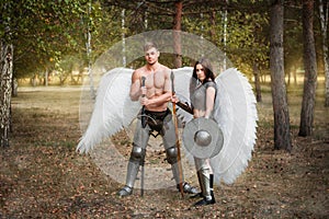 A pair of warrior angels, an athletic man and woman in armor with weapons in their hands and white wings behind their backs