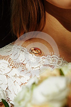 A pair of wedding rings of the bride and groom on the shoulder of the future wife in a white dress. Wedding accessories, ceremony,