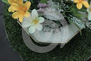 a pair of wedding rings on glass box with flowers