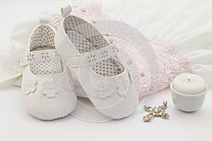 Pair of white baby shoes on embroidered christening white dress, cross and candle