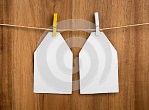 Pair of white carton tags, papers for note, labels for your text or design with clothespins and a rope on a wooden background