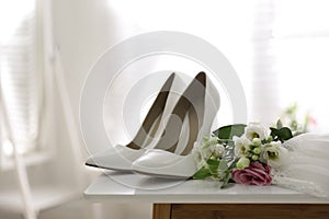 Pair of white high heel shoes, flowers and wedding dress on table indoors