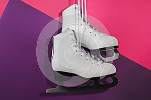 Pair of white ice skates hanging on color background