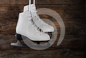 Pair of white ice skates hanging on wooden background. Space for text