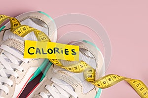 A pair of white sneakers on a pink background and a measuring yellow ribbon, the concept of diet and sports for weight loss