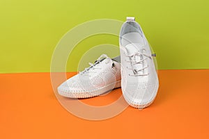 A pair of white summer women`s shoes on a green-orange background