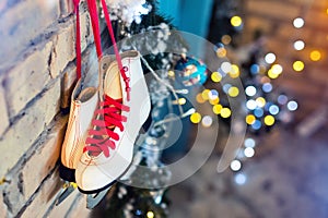 Pair of white vintage leather skates with red laces hanging on old rustic brick wall with blurred lights on christmas