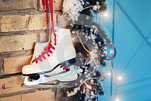 Pair of white vintage leather skates with red laces hanging on old rustic brick wall with garland lights on christmas