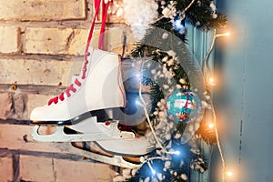 Pair of white vintage leather skates with red laces hanging on old rustic brick wall with glowing garland lights on