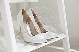 Pair of white wedding high heel shoes on wooden rack indoors  closeup