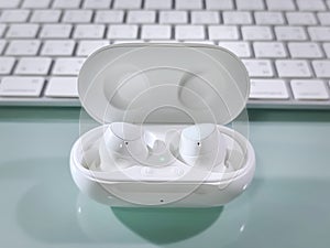 Pair of White Wireless Ear Buds in Dock on Table with Blurred Keyboard Background