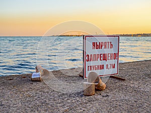 A pair of women`s shoes with heels wallowing on a concrete pier by the sea at sunset in summer. Information board with an