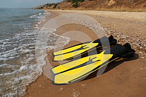 Pair of yellow flippers on sand near sea