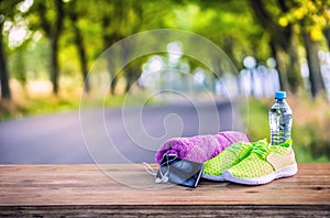 Pair of yellow green sport shoes towel water smart pone and headphones on wooden board. In the background forest or park trail.