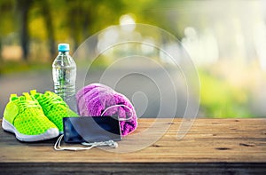 Pair of yellow green sport shoes towel water smart pone and headphones on wooden board. In the background forest or park trail. photo