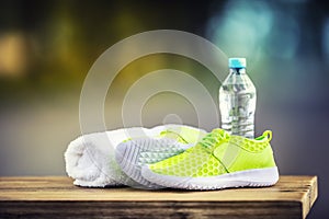 Pair of yellow green sport shoes towel water smart pone and headphones on wooden board. In the background forest or park trail.