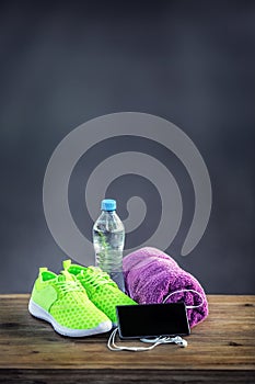 Pair of yellow green sport shoes towel water smart pone and headphones on wooden board. In the background forest or park trail.