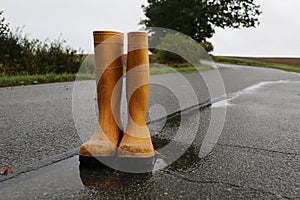 A pair of yellow rubber boots stand in a puddle on the street on a rainy day photo