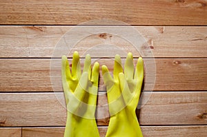 Pair of yellow rubber gloves for cleaning on a wooden floor, background cpoy space.