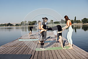 A pair yoga class with an instructor on a wooden pier on the river in the city. A group of women train outdoors in the morning