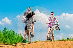 Pair of young cyclists on the hill against the sky