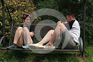 A pair of young people talking on a garden swing.