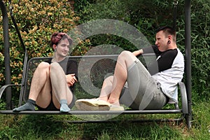 A pair of young people talking on a garden swing.