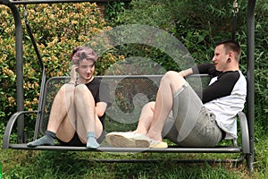 A pair of young people talking on a garden swing.