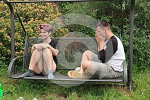 A pair of young people talking on a garden swing.