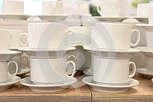 Pairs of mugs and plates on shelf of the tableware store. A lot of rows of pure white cups with plates for coffee break