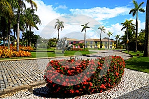 Paisagismo tropical com jardins, construÃ§Ãµes coloridas ao fundo cercadas por muita vegetaÃ§Ã£o