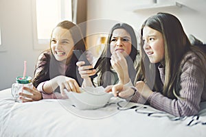 A pajama party with teens eat popcorn on the bed