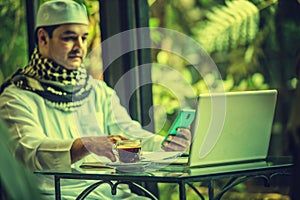 Pakistani muslim Man working on laptop and cellphone in cafe