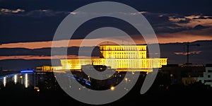 The Palace of the Parliament Palatul Parlamentului in Romanian in Bucharest, Romania, illuminated at night, among dark clouds.