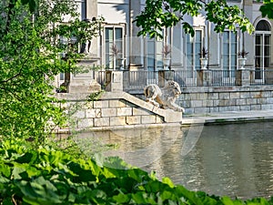 Palace on the water, a fragment of a terrace with a sculpture of a lion. View from under the branches of trees on a summer day.