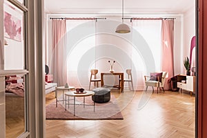 Pale pink living room interior in tenement house, real photo with copy space on the empty white wall and parquet on the floor