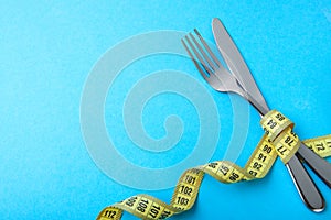 Paleo diet for weight loss. The fork and knife are wrapped in yellow measuring tape on blue