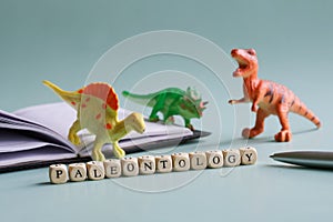 Paleontology inscription next to toy dinosaurs and an open notebook. Concept for studying cryptozoology, zoology and dinosaurs in