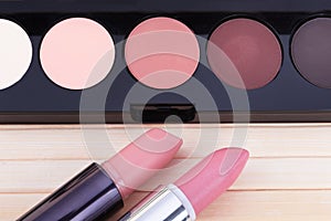 A palette with beige,pink,black,white eye shadows and two lipsticks of brown and pale pink colors.Soft focus.Concept of choosing
