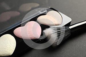 Palette of heart shaped eyeshadows with brush on dark background, closeup