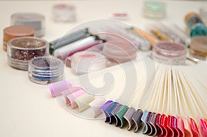 Palette of nail design of different colors with gel polish on white tips and background, jars with sparkles and decor