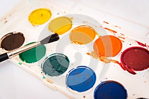 Palette of watercolor paint and one brush on white sheets of paper