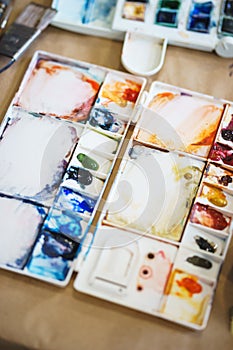 Palette with watercolors in different colors. Various brushes and pencils for drawing prepared by the artist for work.