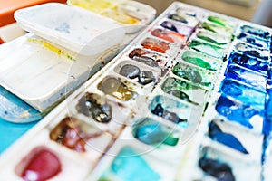 Palette with watercolors in different colors. Various brushes and pencils for drawing prepared by the artist for work.